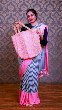 Woman in a saree holding a pink bag against a patterned wall.