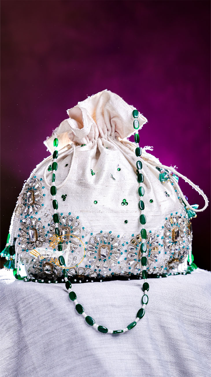 Decorative white drawstring bag with green beads on a purple background