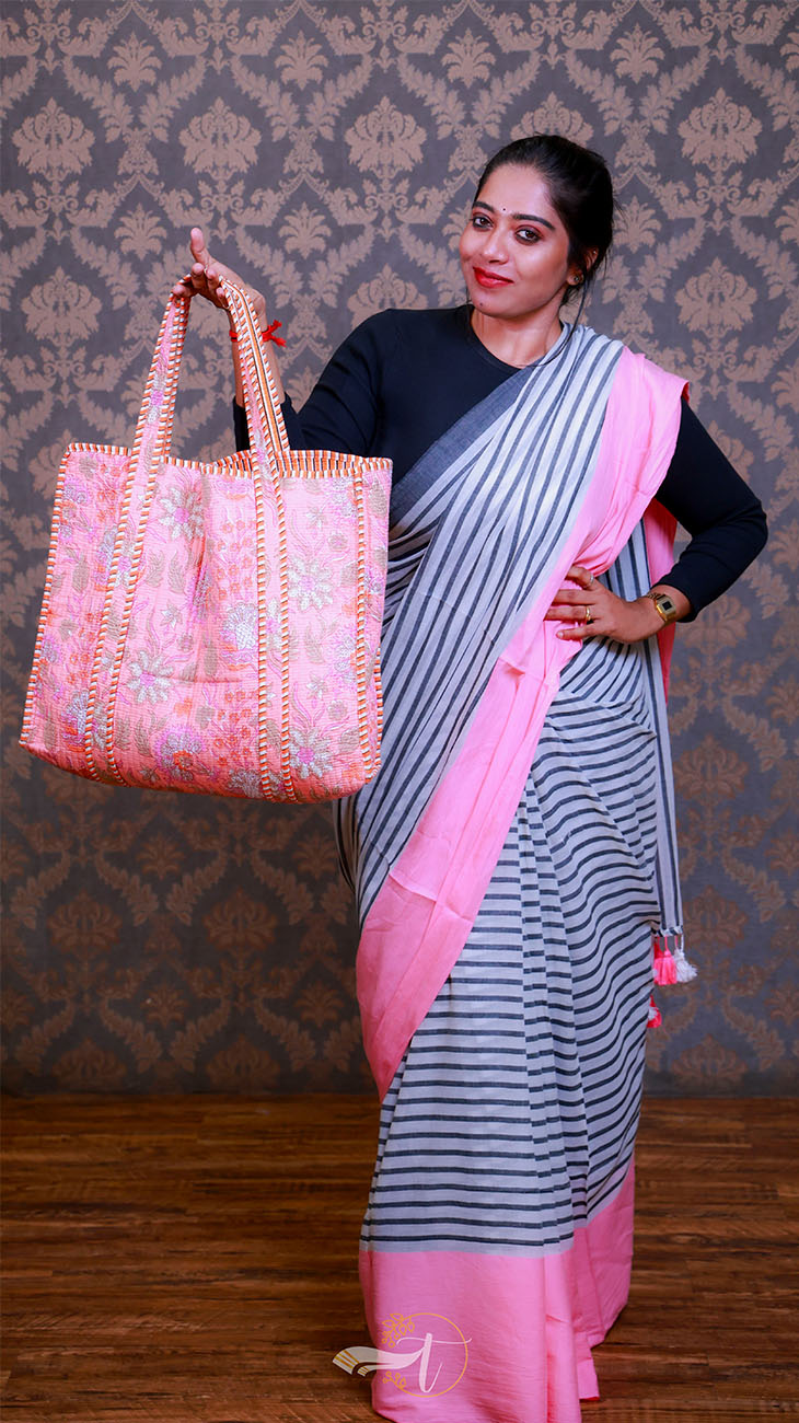 Woman holding a pink embroidered bag against a patterned wall.