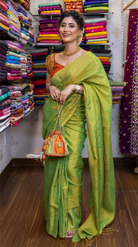 Woman in a green saree standing in front of a colorful fabric display.
