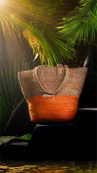 Woven bag with brown top and orange bottom on a dark surface with green foliage in the background