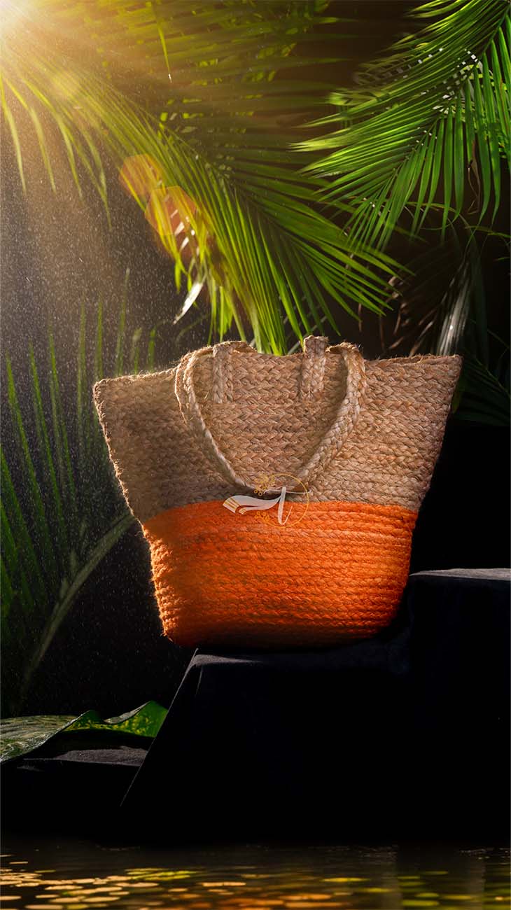 Woven bag with brown top and orange bottom on a dark surface with green foliage in the background
