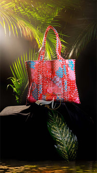 Colorful woven bag on a dark surface with green foliage in the background