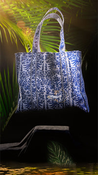 Blue patterned tote bag on a dark surface with green foliage in the background
