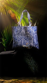 Blue and white patterned tote bag on a dark background with palm leaves