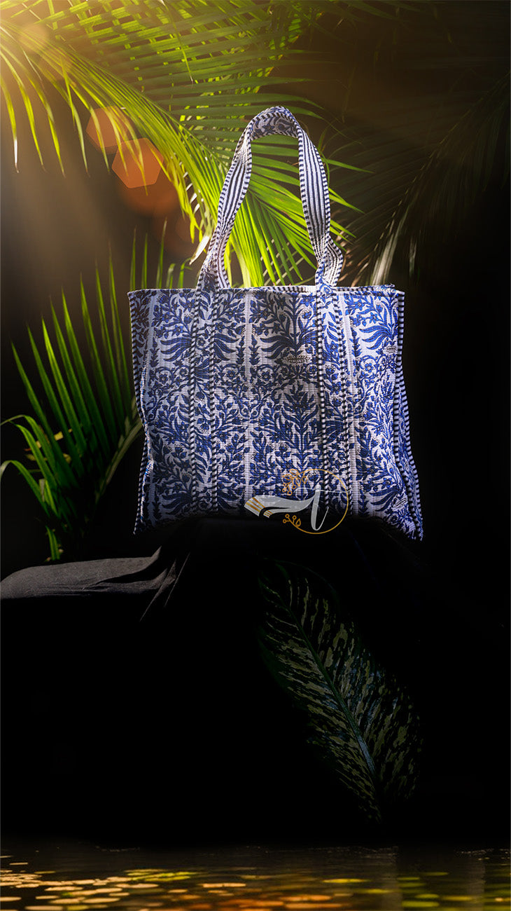 Blue and white patterned tote bag on a dark background with palm leaves