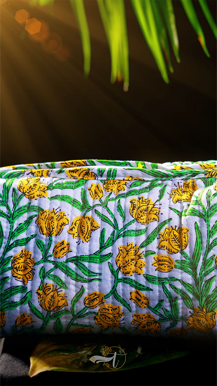 Embroidered fabric with yellow flowers on a green background, sunlit with palm leaves in the background.