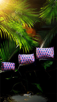 Decorative cushions with a pink and blue pattern on a dark background with green leaves.