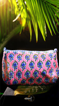 Pink pouch with blue floral pattern against a dark background with green leaves