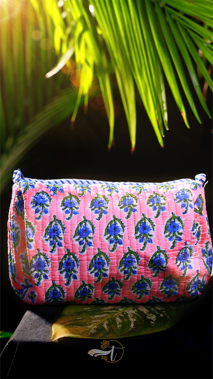 Pink pouch with blue floral pattern against a dark background with green leaves