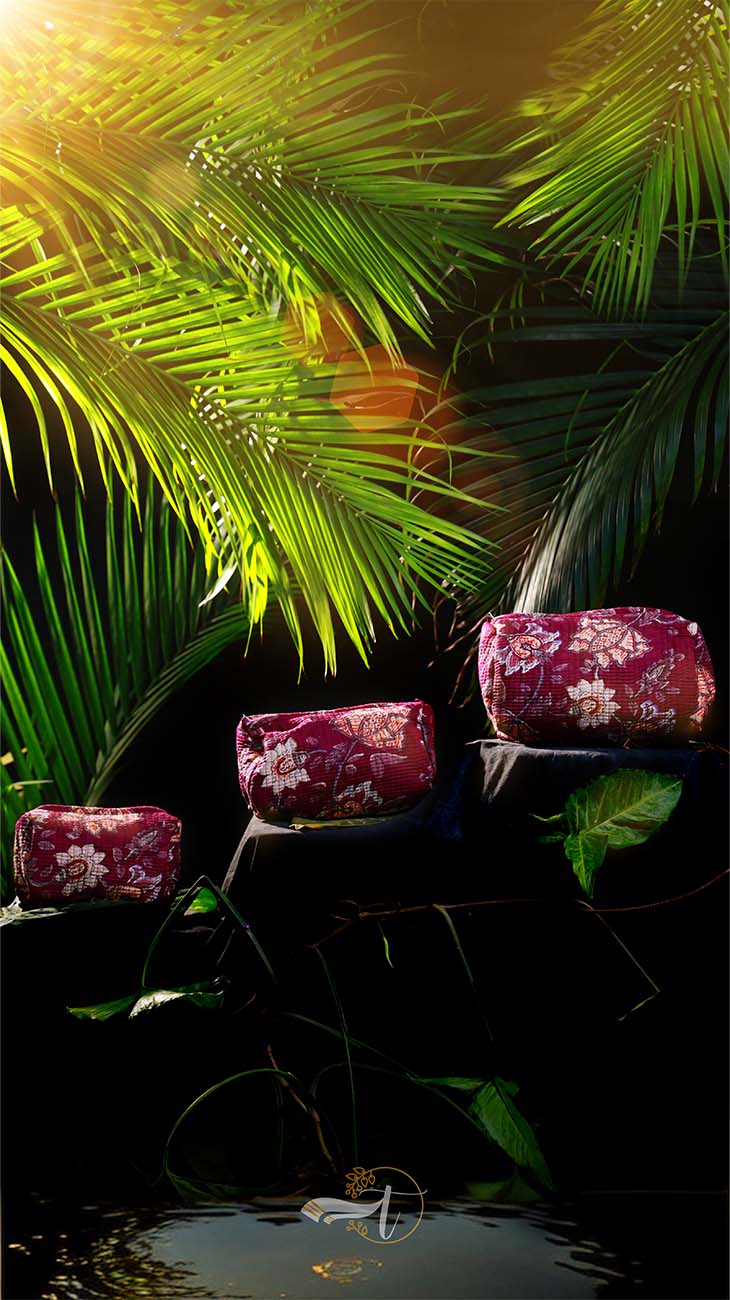 Red floral cushions on a chair surrounded by green foliage with sunlight filtering through.