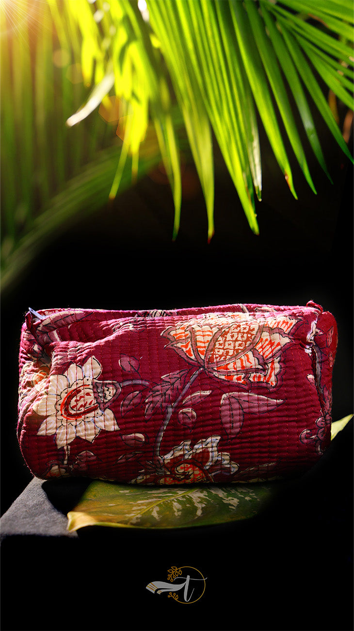 Red floral clutch bag on a dark surface with green leaves in the background