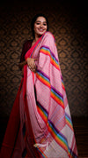 Woman wearing a pink saree with rainbow stripes against a patterned wall.
