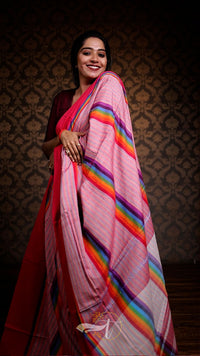 Woman wearing a pink saree with rainbow stripes against a patterned wall.