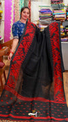 Woman holding a black saree with red patterns in a fabric store.