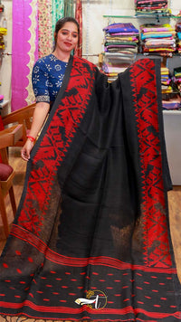 Woman holding a black saree with red patterns in a fabric store.