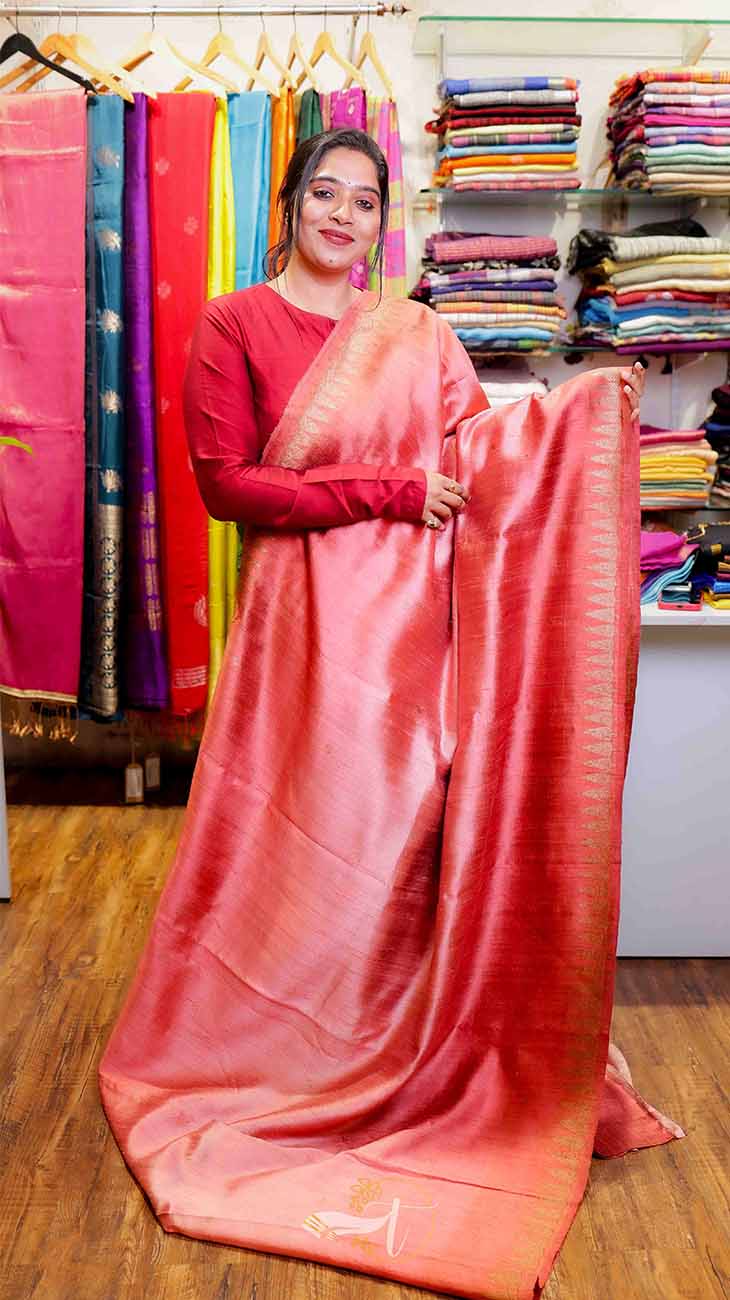 Woman holding a pink saree in a fabric store with colorful fabrics in the background.