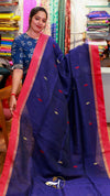 Woman wearing a blue saree with red border in a fabric store.