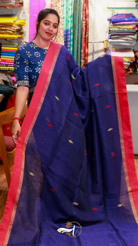Woman wearing a blue saree with red border in a fabric store.