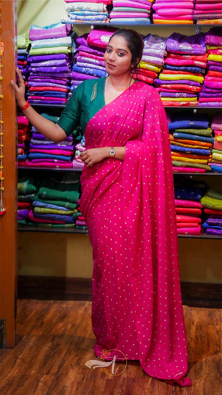 Woman in a bright pink saree standing in front of a colorful fabric display.