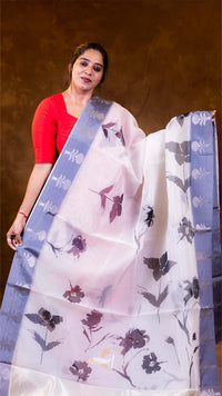 Woman holding a white saree with floral patterns against a brown background