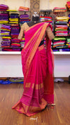 Pink saree with gold border on a mannequin against a background of colorful fabrics.