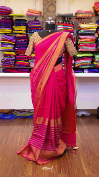 Pink saree with gold border on a mannequin against a background of colorful fabrics.