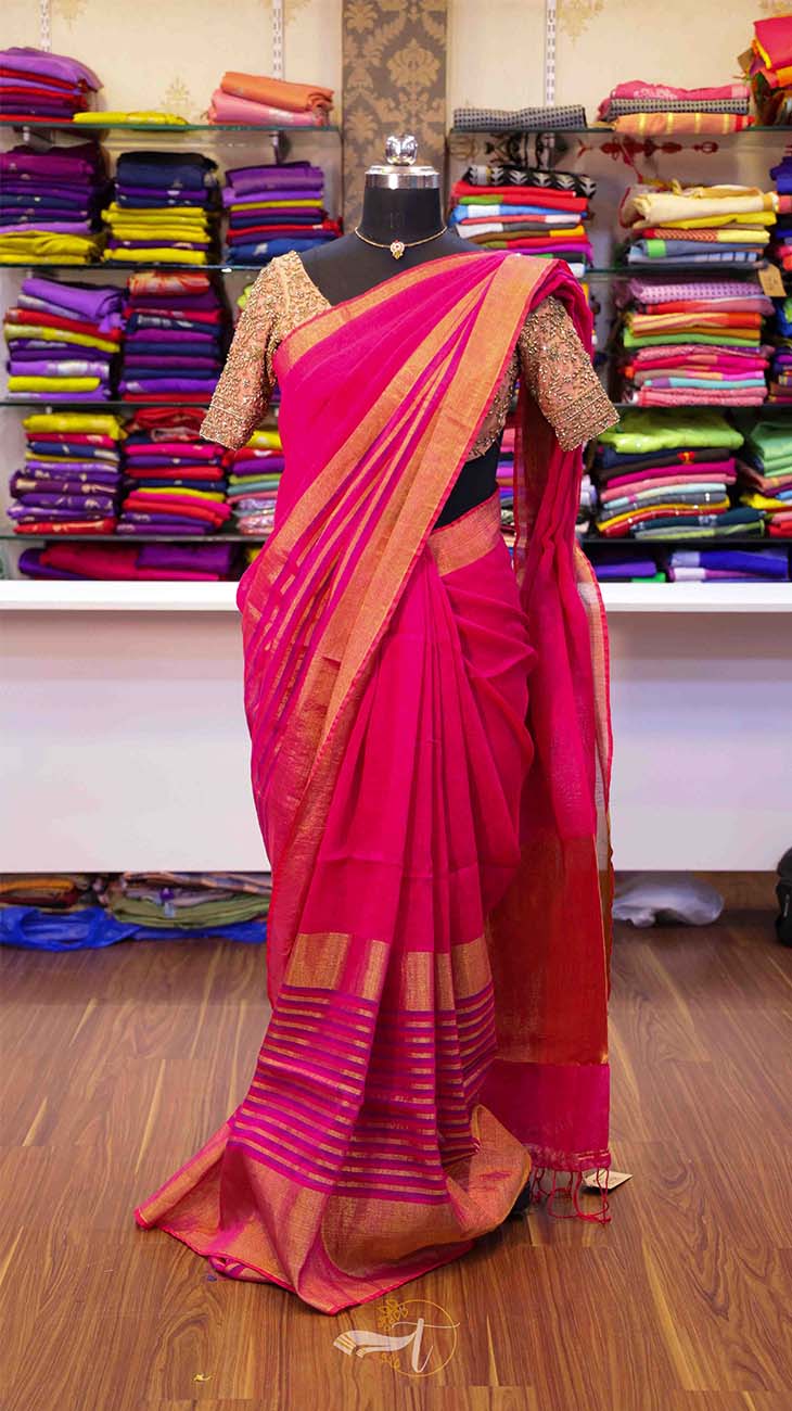 Pink saree with gold border on a mannequin against a background of colorful fabrics.