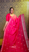 Woman in a bright pink saree with a decorative pattern against a patterned wall.