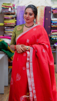 Woman wearing a red saree with a green blouse in a fabric store.