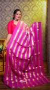 Woman wearing a pink saree with gold stripes against a patterned wall.
