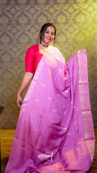 Woman in a pink saree with a red blouse against a patterned wall.