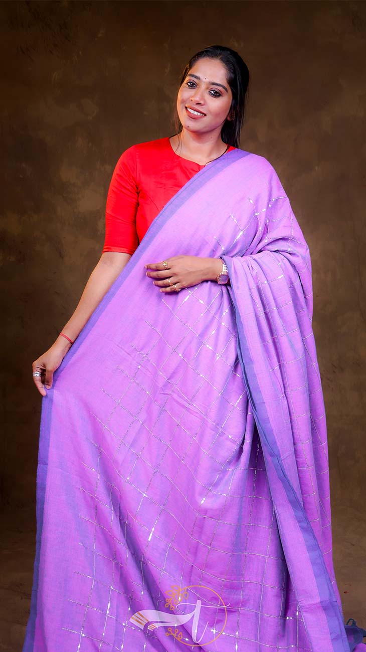 Woman wearing a purple saree with a red blouse against a brown background