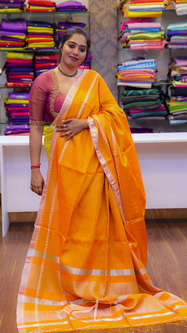 Woman in a yellow saree standing in a fabric store with colorful sarees in the background.