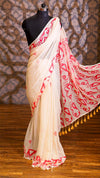 White saree with red patterns on a mannequin against a patterned wall.