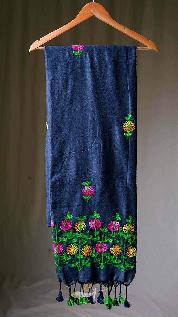 Dark blue fabric with colorful floral embroidery on a wooden hanger against a neutral background