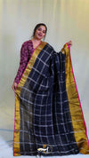 Woman holding a black checkered saree with gold border against a white background