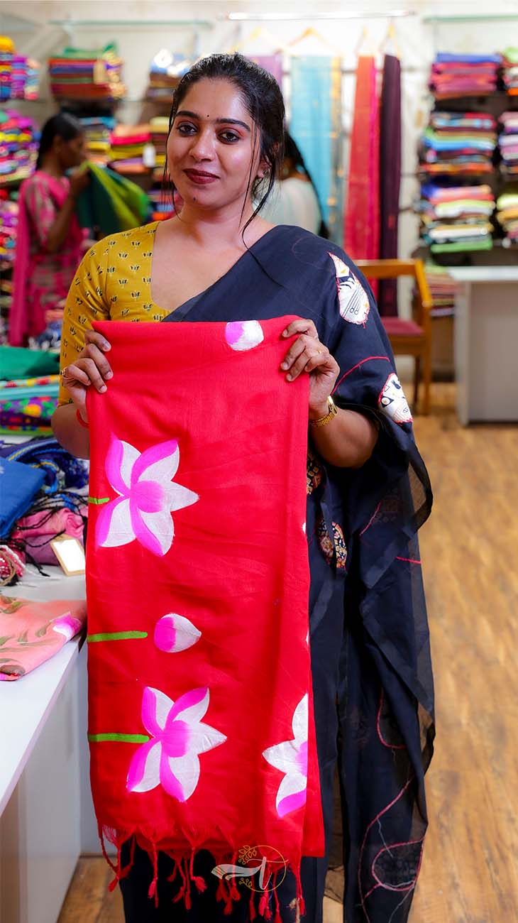 Woman holding a red scarf with floral patterns in a fabric store.