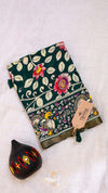 Decorative notebook with floral design and a small black pot on a light background