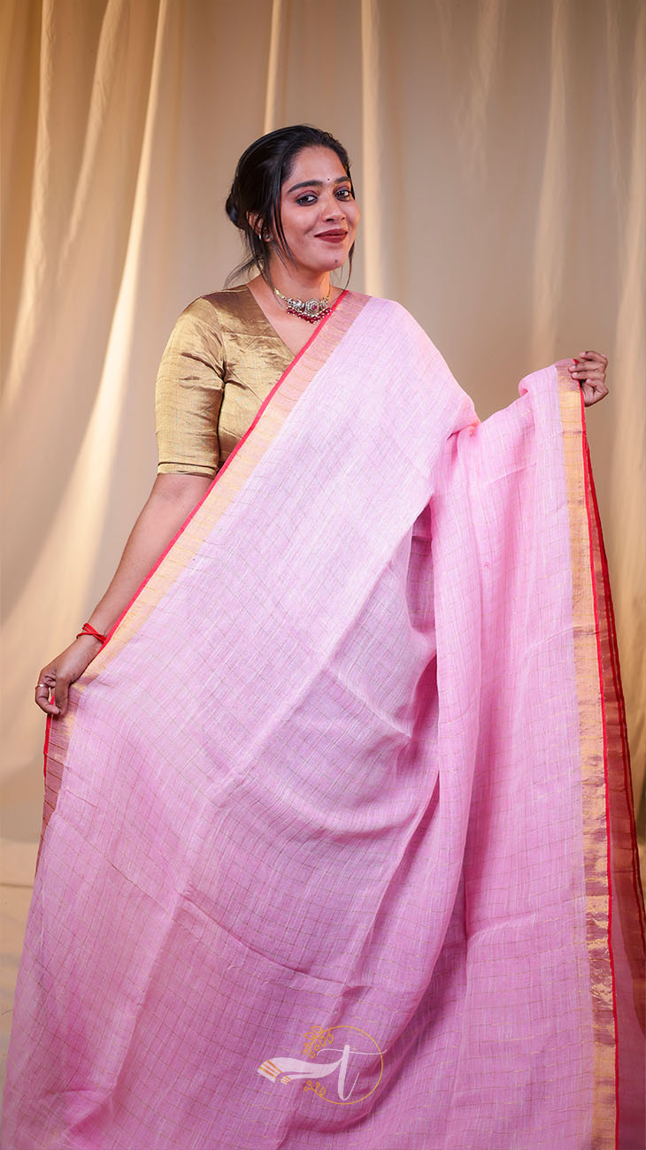 Woman wearing a pink saree with a gold blouse against a beige curtain background