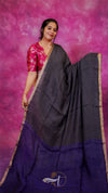Woman wearing a black and purple saree with a pink blouse against a pink background
