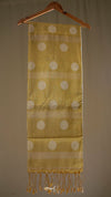 Yellow scarf with white polka dots and fringes hanging on a wooden hanger against a beige background