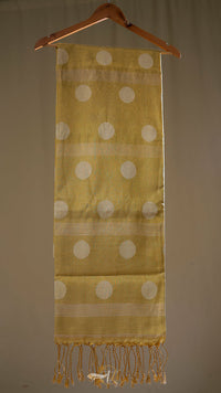 Yellow scarf with white polka dots and fringes hanging on a wooden hanger against a beige background