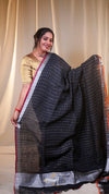 Woman wearing a black checkered saree with a red border against a beige curtain background