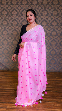 Woman wearing a pink saree with heart patterns against a patterned wall.
