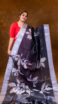 Woman holding a dark purple saree with white floral patterns against a brown background