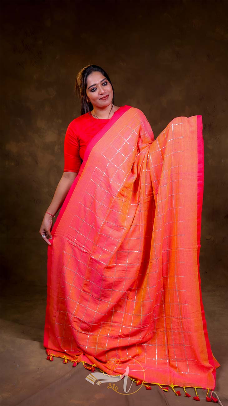 Woman wearing a bright orange saree with a red blouse against a brown background