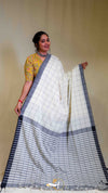 Woman wearing a white saree with black checks and a yellow blouse against a beige background