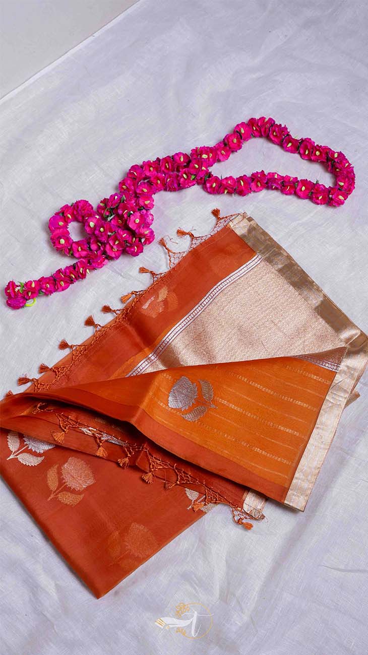 Orange saree with gold border and pink beaded necklace on a light gray background