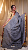 Woman wearing a gray saree with a red border against a beige curtain background